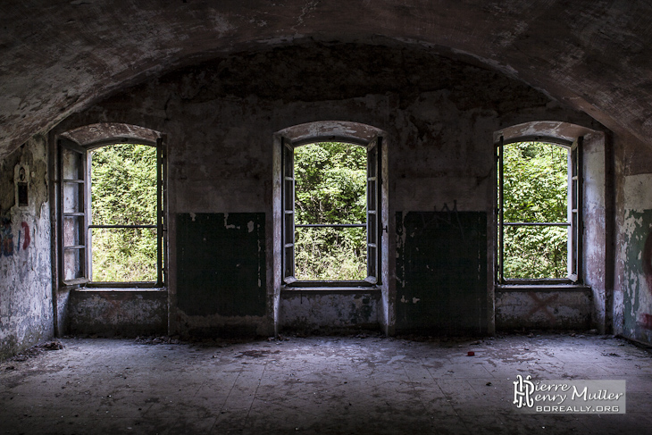 Intérieur d'une pièce de la caserne avec trois fenêtres au Fort du Haut Buc