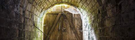 ...La sortie d’un tunnel du fort du Trou d’Enfer fermée par une porte en bois laissant passer la lumière extérieure....