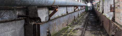 ...Une passerelle inter niveau de la papeterie avec tuyaux et câbles électriques. Les rails au sol permettent le passages des wagons berlines de la papeterie....