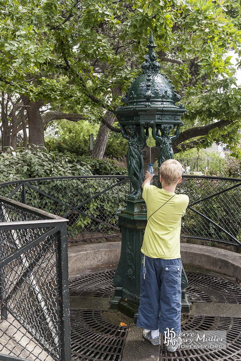 Enfant remplissant une gourde d'eau à la fontaine Wallace de la butte Montmatre