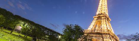 ...Champs de Mars avec des personnes en train de picniquer et Tour Eiffel illuminée au coucher de soleil sur fond de ciel bleu....