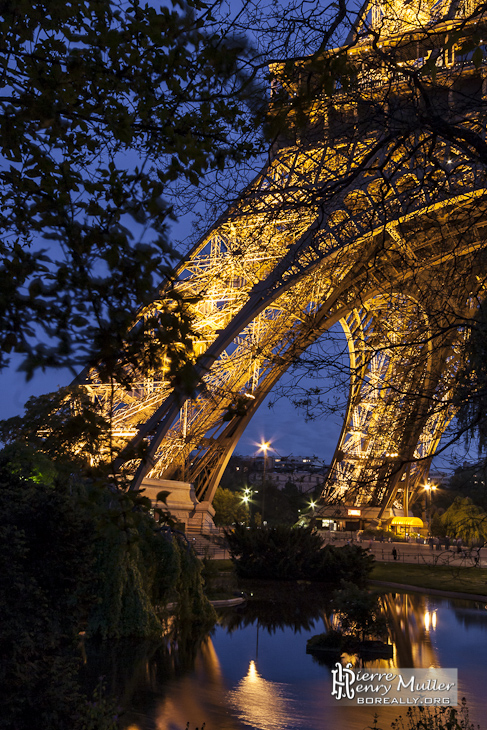 Pieds de la Tour Eiffel et reflet sur le plan d'eau de nuit
