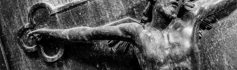 ...Sculture de Jesus sur sa croix en noir et blanc sur la porte d’un caveau....